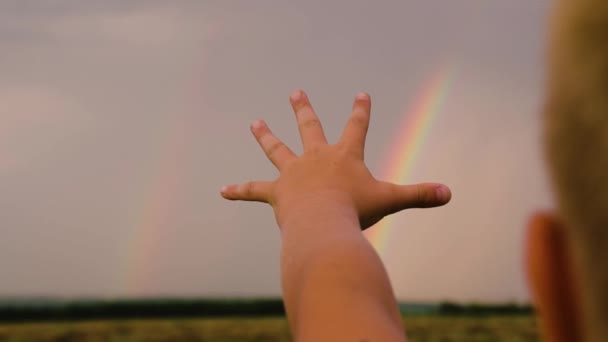The child dreams of touching a multi-colored rainbow in the sky. Happy family concept. Happy child, boy stretches out his hand to the rainbow against the blue sky. Family walks in the park after rain. - Footage, Video