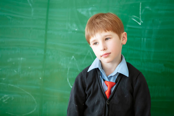 Sad Student child in class. Schoolboy at the green blackboard with a boring face. Education problems in primary grades.Didn't learn the lesson - Photo, Image