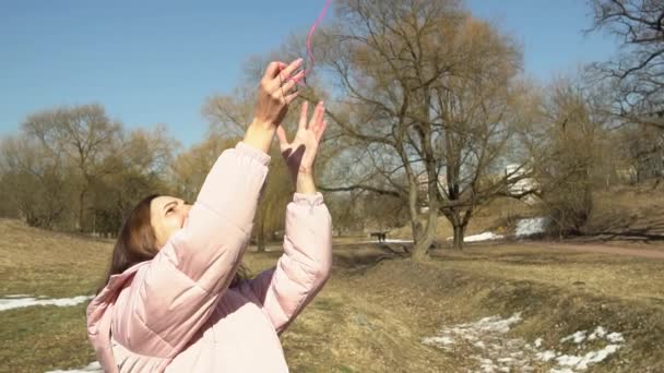 Una ragazza in giacca rosa lancia una palla di fili in un parco primaverile autunnale al rallentatore - Filmati, video