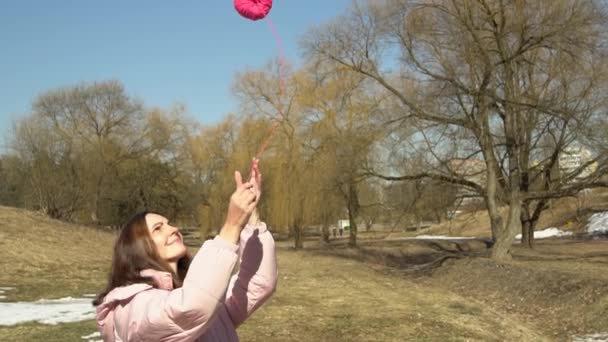 Uma menina em uma jaqueta rosa lança uma bola de fios em um parque de primavera outono câmera lenta - Filmagem, Vídeo
