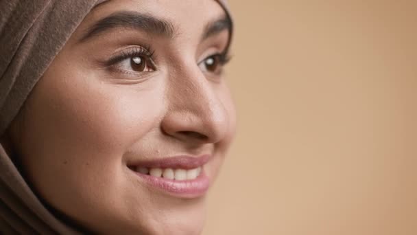 Мусульманка в хиджабе улыбается, глядя в сторону, бежевый фон, крупный план - Кадры, видео