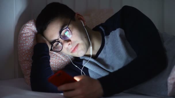 Yatakta kulaklık takmış ve gece biriyle mesajlaşan genç bir adamın yakın çekimi. Gece yazışmaları - Video, Çekim