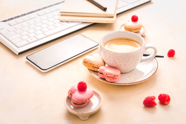 Feminine business workplace with keyboard, writing supplies, cup of coffee and small macarons in bright tone - 写真・画像