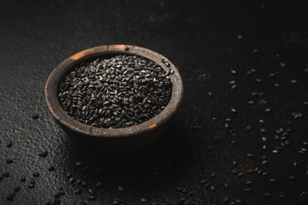 Czarne nasiona sezamu w małej misce na czarnym tle - Zdjęcie, obraz