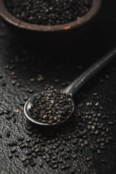 Black sesame seeds in small bowl on black background - Foto, Bild