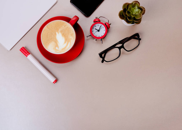 red cup of coffee, pen, glasses, alarm,  plant, phone, paper on beige background - Foto, imagen