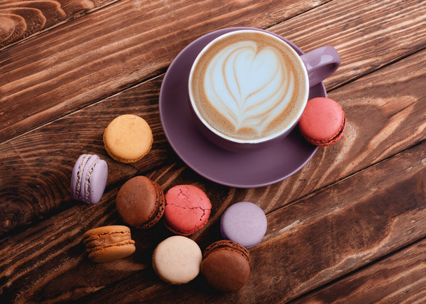 Fioletowy kubek kawy z sercem i kolorowe makaroniki na drewnianym tle - Zdjęcie, obraz