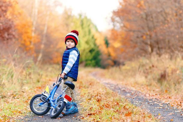 Petit garçon en vêtements chauds colorés dans le parc forestier d'automne conduisant un vélo - Photo, image