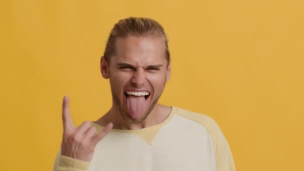 Emotionaler junger Kerl zeigt Rock "n" Roll-Geste und streckt die Zunge heraus - Filmmaterial, Video