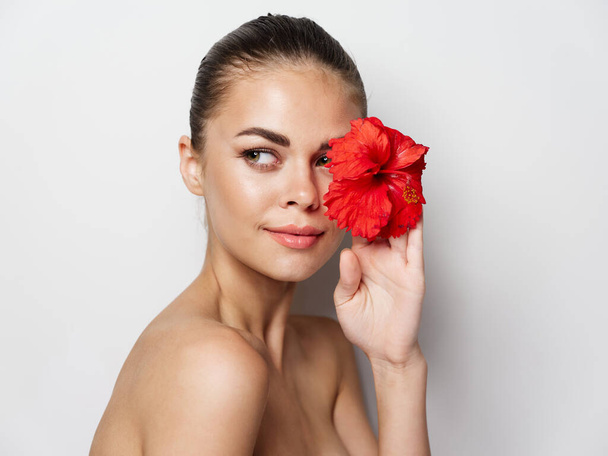 young woman with red flower in hand clear skin bare shoulders  - Фото, изображение