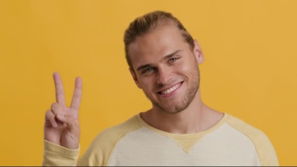 Vrolijke jonge man toont vrede gebaar terwijl poseren over gele Studio achtergrond - Video
