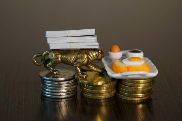 Een metalen tijger en een speelgoedbakje met een kop koffie en een broodje op een stapel munten. Bedrijfsconcept. - Foto, afbeelding