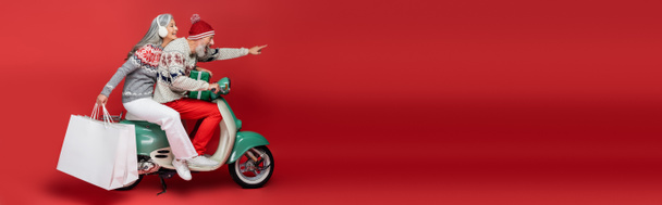 allegra donna asiatica di mezza età che tiene borse della spesa mentre cavalca ciclomotore con marito che punta il dito sul rosso, striscione - Foto, immagini