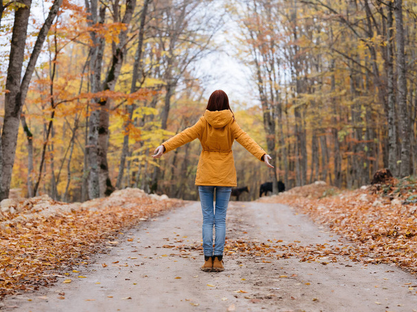 woman outdoors in a yellow jacket walks in the autumn forest road - Fotó, kép