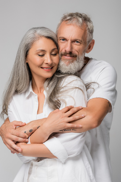 happy and interracial mature couple hugging isolated on grey - Valokuva, kuva