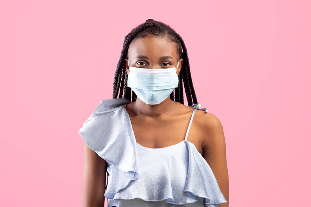 Ochrona przed koronawirusami. Młoda czarna kobieta w ochronnej medycznej masce twarzy patrząc na kamerę na różowym tle - Zdjęcie, obraz