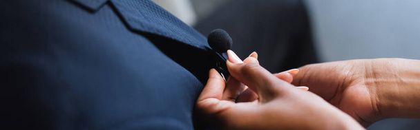 vista cortada de assistente americano africano ajustando microfone em terno de homem de negócios, banner - Foto, Imagem