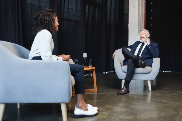 wazig Afrikaans-Amerikaanse journalist lacht en praat met zakenman tijdens talkshow  - Foto, afbeelding
