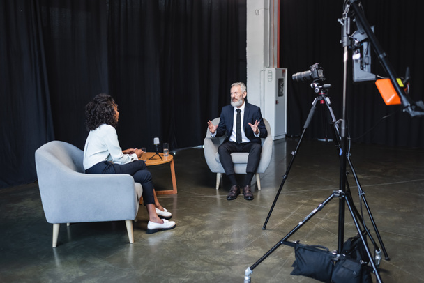 krullend Afrikaans amerikaanse journalist praten met zakenman in interview studio  - Foto, afbeelding