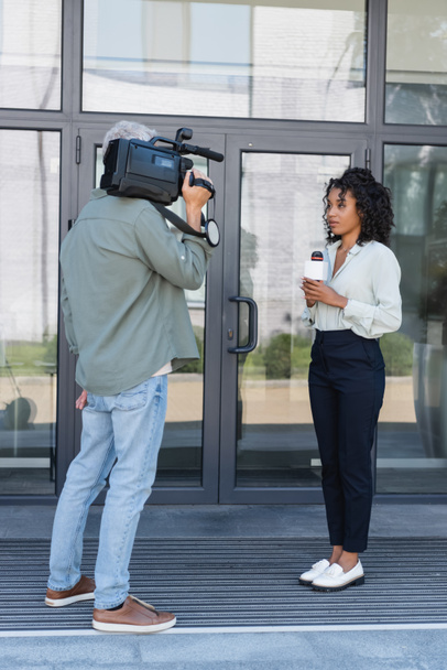 pełna długość amerykańskiego dziennikarza afrykańskiego robi reportaż w pobliżu kamerzysty na zewnątrz - Zdjęcie, obraz