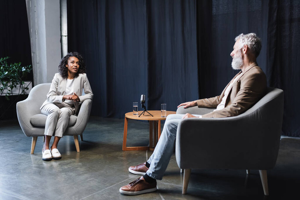 afro-amerikai újságíró beszél szakállas üzletemberrel, aki karosszékben ül az interjú alatt. - Fotó, kép
