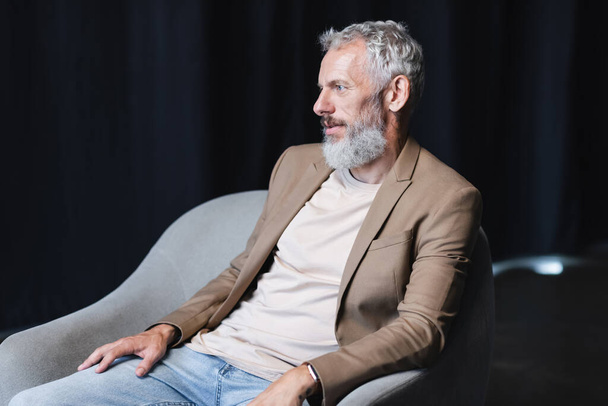 インタビュー中に灰色のアームチェアに座っている髭のビジネスマンは - 写真・画像