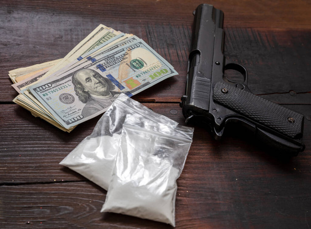 Drogas narcóticos concepto de negocio ilegal. Paquetes de plástico de cocaína, pistolas y billetes en dólares estadounidenses en una mesa. Polvo blanco adicción y crimen - Foto, Imagen