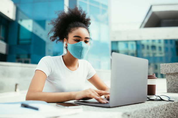 nero ragazza a computer portatile guardando online lezione indossando maschera all'aperto - Foto, immagini