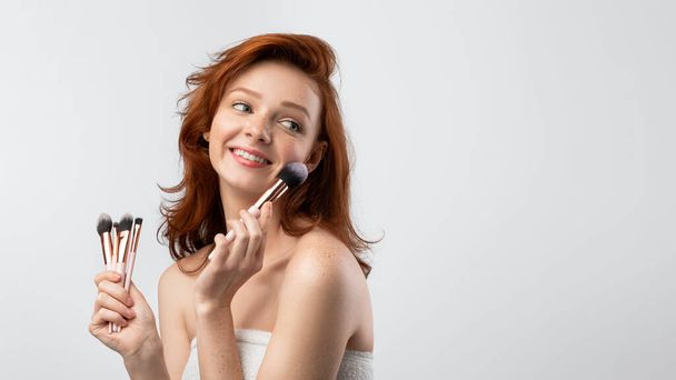 Red-Haired Young Female Holding Cosmetic Brushes Near Face - Фото, зображення