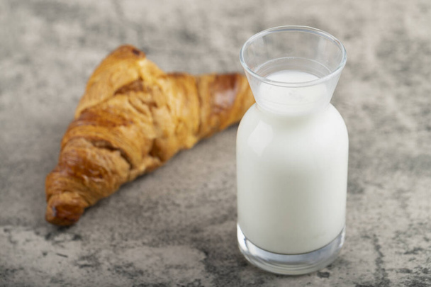 Sabroso croissant mantecoso con una jarra de vidrio de leche fresca colocada en la mesa de piedra. Foto de alta calidad - Foto, Imagen