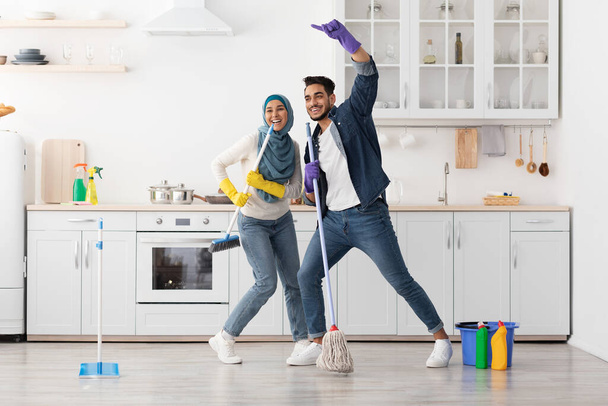 Šťastný muslim pár úklid podlahy a baví v kuchyni - Fotografie, Obrázek