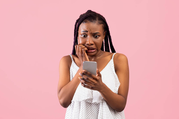 Vystrašená černoška se dívá na smartphone v hrůze, vidí špatné zprávy, fotografie nebo vzkaz na růžovém pozadí - Fotografie, Obrázek
