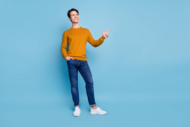 Photo of promoter guy indicate forefinger empty space wear orange shirt jeans shoes isolated blue color background - Фото, зображення