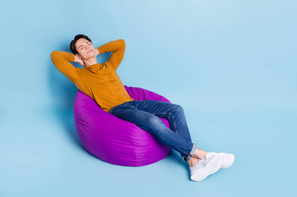 Full body photo of comfy brunet young guy sit on bag wear sweater jeans isolated on blue color background - Fotografie, Obrázek