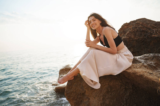 Woman traveler sitting near sea on cliff injoying view of sea and nature - Photo, Image