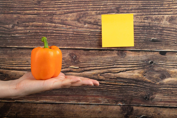 Female hand holding orange colored bell pepper on wooden background. High quality photo - Zdjęcie, obraz