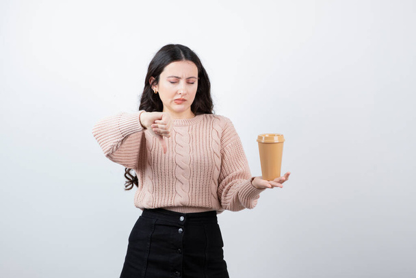 Young brunette woman showing thumb down and holding a cup of hot coffee . High quality photo - Photo, Image