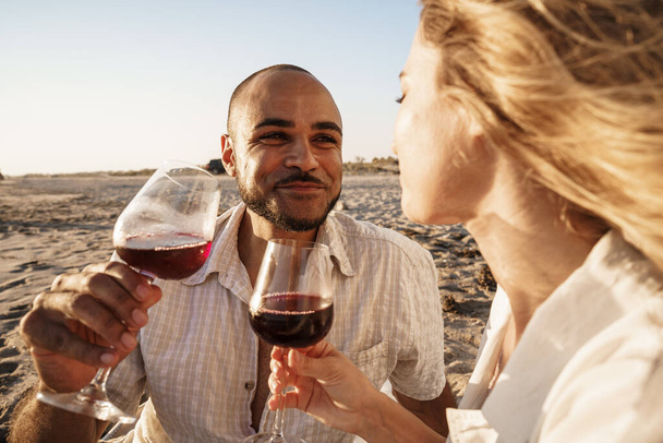 Portrait of a young couple sitting on the beach and drinking wine - 写真・画像