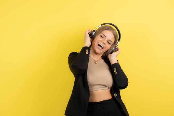 Hermosa mujer en auriculares escuchando canciones sobre fondo amarillo. Foto de alta calidad - Foto, Imagen