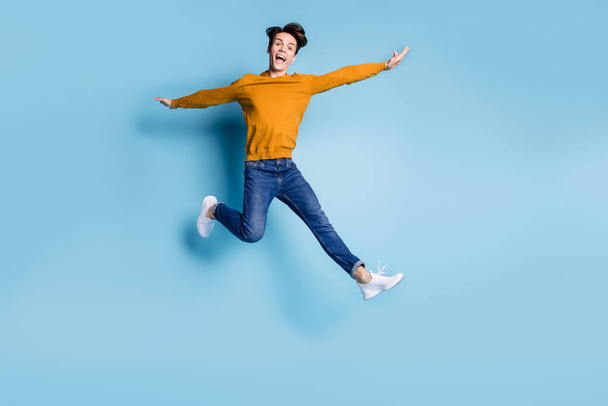 Full length photo of joyful brunet young guy jump yell wear sweater jeans isolated on blue color background - Foto, Bild
