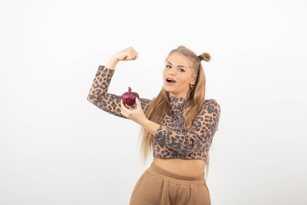 Image of young woman in crop top holding red onion and standing over white. High quality photo - Photo, Image