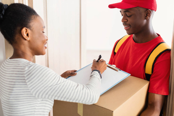 African Woman Signing Papers Receiving Parcel From Courier At Home - Photo, Image
