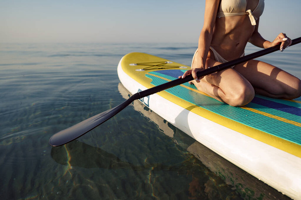 Close up of young woman sitting on a stand up paddle board - Foto, Imagen