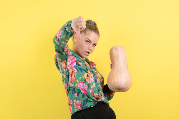 Image of a woman with fresh butternut squash showing thumb down against yellow wall . High quality photo - Fotó, kép