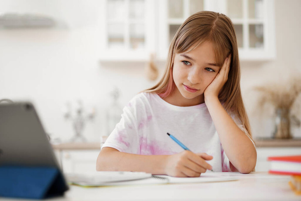 Teenage κορίτσι κρατώντας σημειώσεις στο σημειωματάριο, κάνει την εργασία στο τραπέζι στο σπίτι - Φωτογραφία, εικόνα