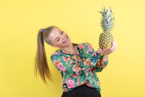 Niesamowita młoda kobieta ze świeżym ananasem, pozująca na żółtą ścianę. Wysokiej jakości zdjęcie - Zdjęcie, obraz