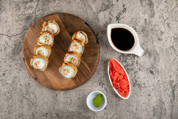 Wooden board of hot fried sushi rolls with salmon and sauces on stone surface. High quality photo - Valokuva, kuva