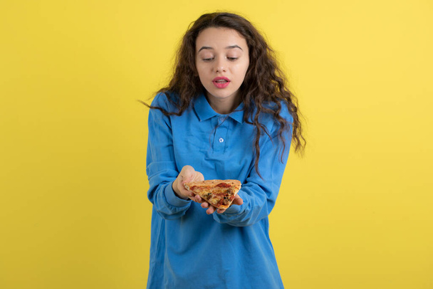 Photo of beautiful young girl with piece of pizza posing on yellow background. High quality photo - Photo, Image