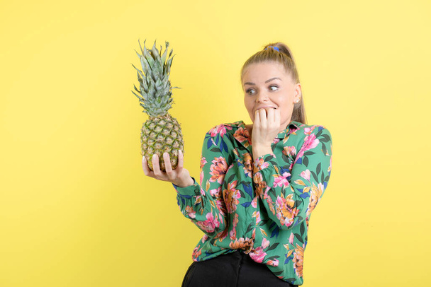 Incroyable jeune femme avec de l'ananas frais posant contre un mur jaune. Photo de haute qualité - Photo, image