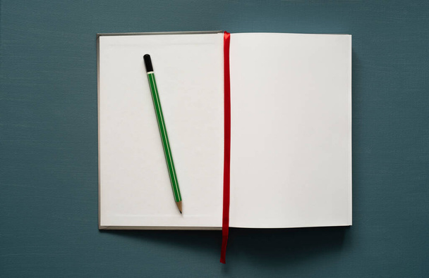 notebook hely szöveges, zöld ceruza, piros könyvjelző, sötét türkiz háttér, fénykép felülről - Fotó, kép